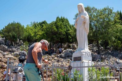Anciano rezando frente a la estatua de La Virgen en la colina de las apariciones (Monte Podbrdo) de Medjugorje (Bosnia)