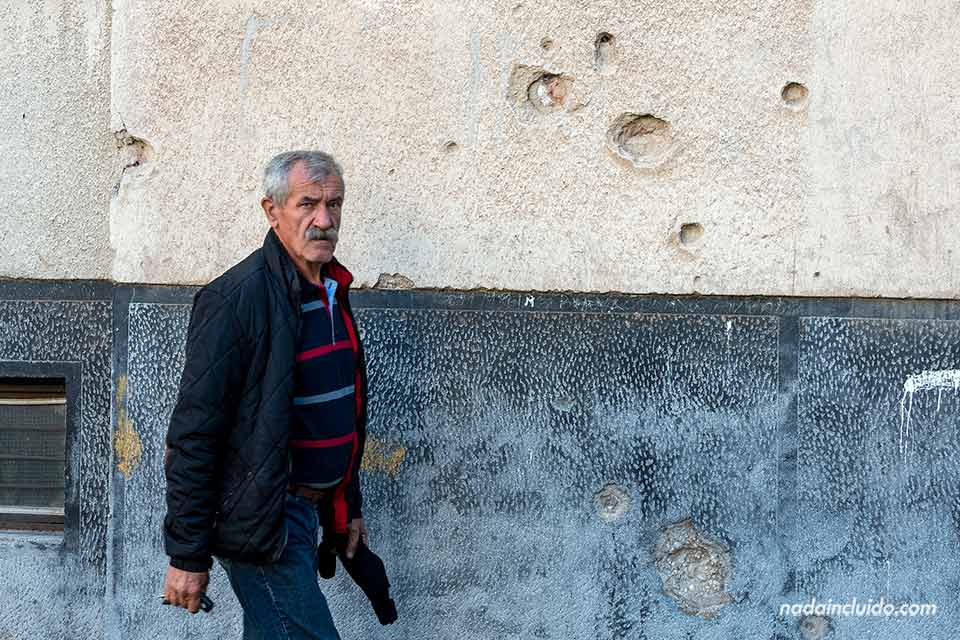 Un hombre camina junto a una fachada dañada por las balas en Mostar (Bosnia)